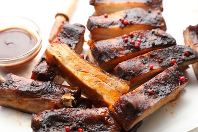 Photo of Delicious pork ribs and sauce on parchment paper, closeup