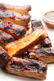 Photo of Delicious pork ribs and sauce on parchment paper, closeup