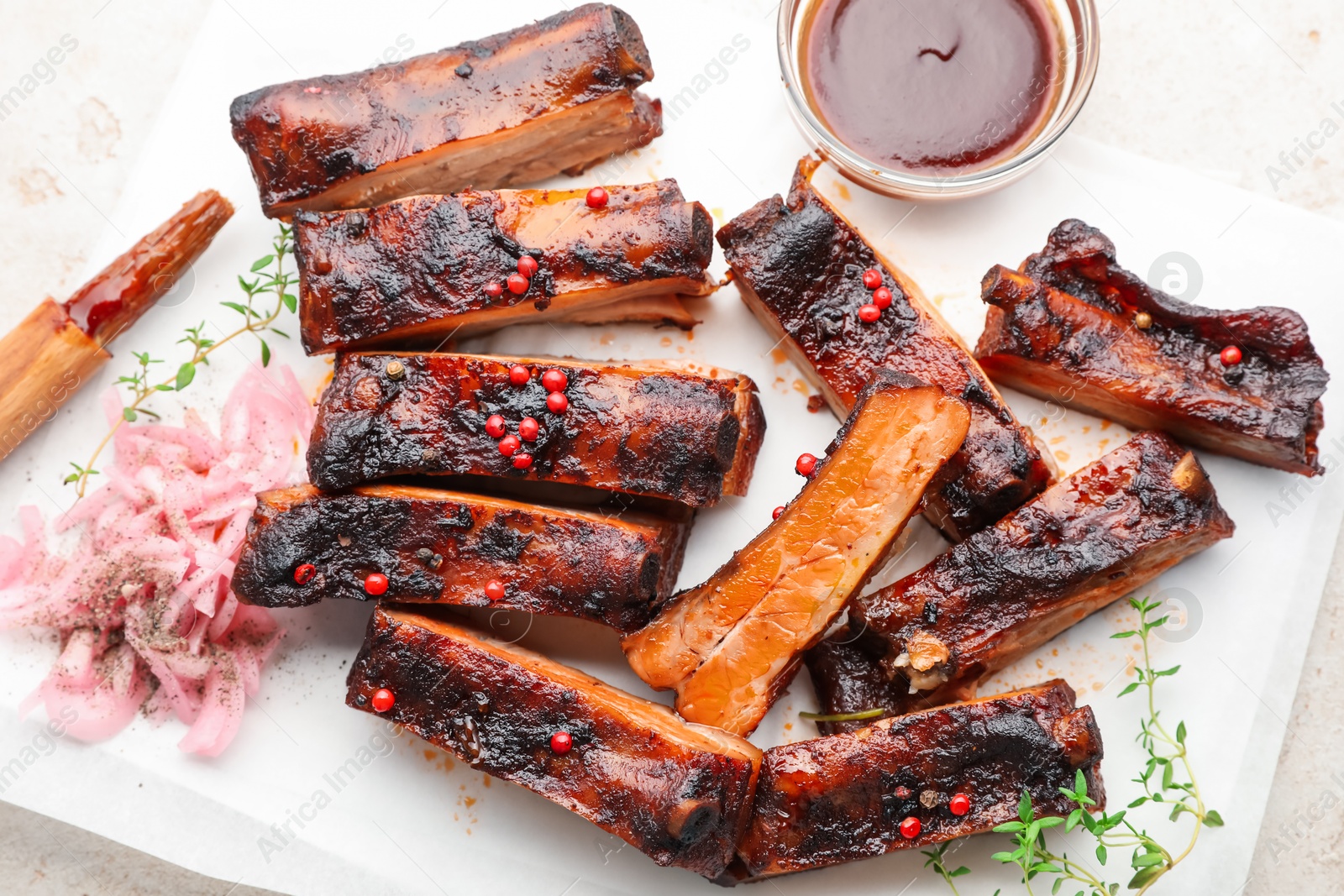 Delicious pork ribs, thyme, onion, sauce and brush on light table, flat lay Photo of Delicious pork ribs, thyme, onion, sauce and brush on light table, flat lay