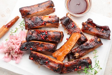 Photo of Delicious pork ribs, thyme, onion, sauce and brush on light table, flat lay