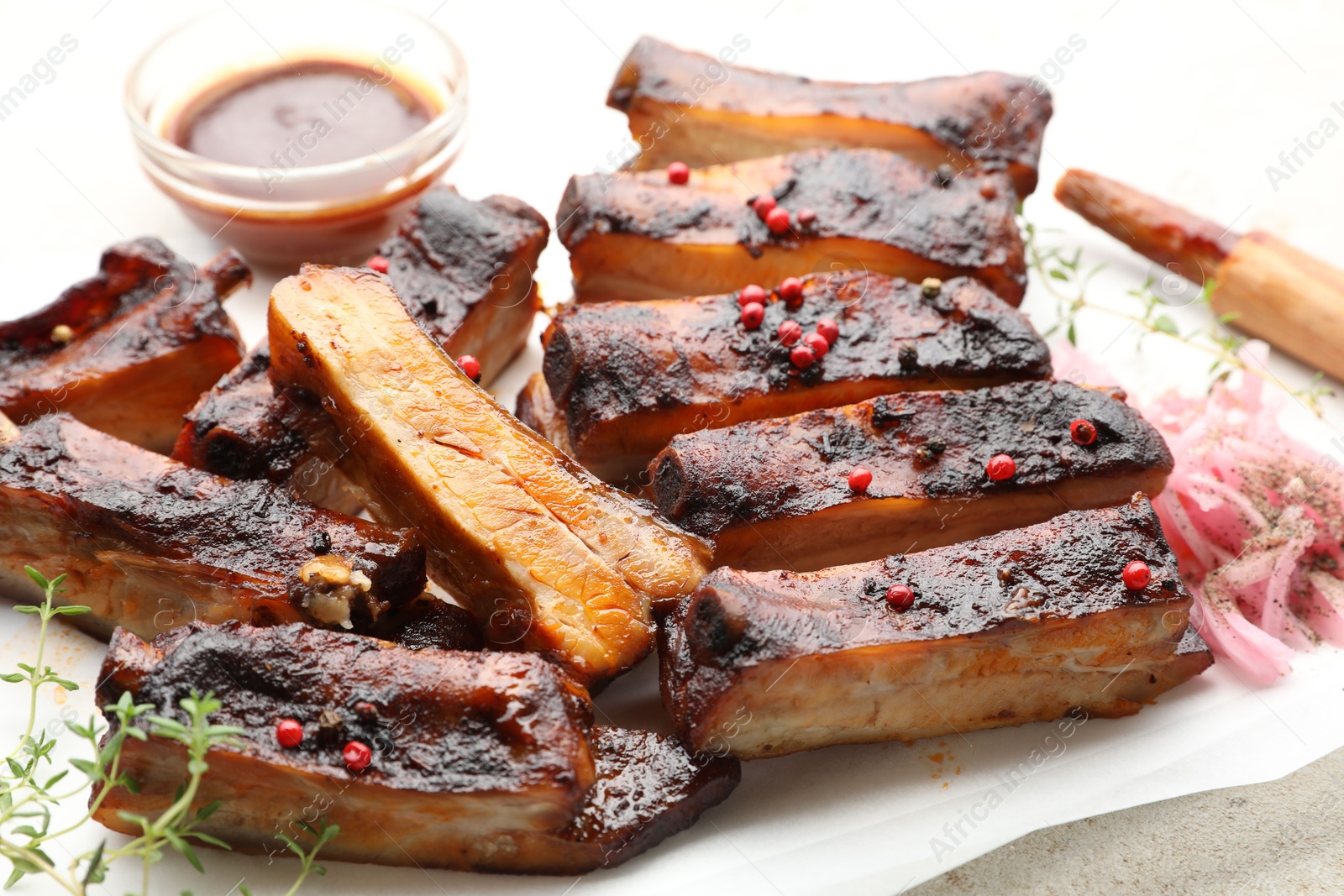 Delicious pork ribs, thyme, onion, sauce and brush on light table, closeup Photo of Delicious pork ribs, thyme, onion, sauce and brush on light table, closeup