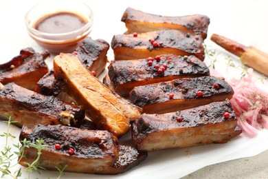 Photo of Delicious pork ribs, thyme, onion, sauce and brush on light table, closeup