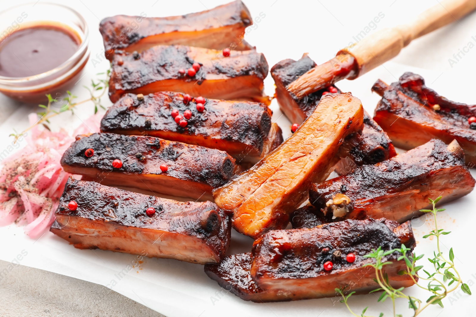 Delicious pork ribs, thyme, onion, sauce and brush on light table, closeup Photo of Delicious pork ribs, thyme, onion, sauce and brush on light table, closeup