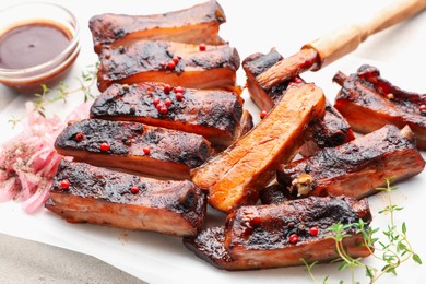 Photo of Delicious pork ribs, thyme, onion, sauce and brush on light table, closeup