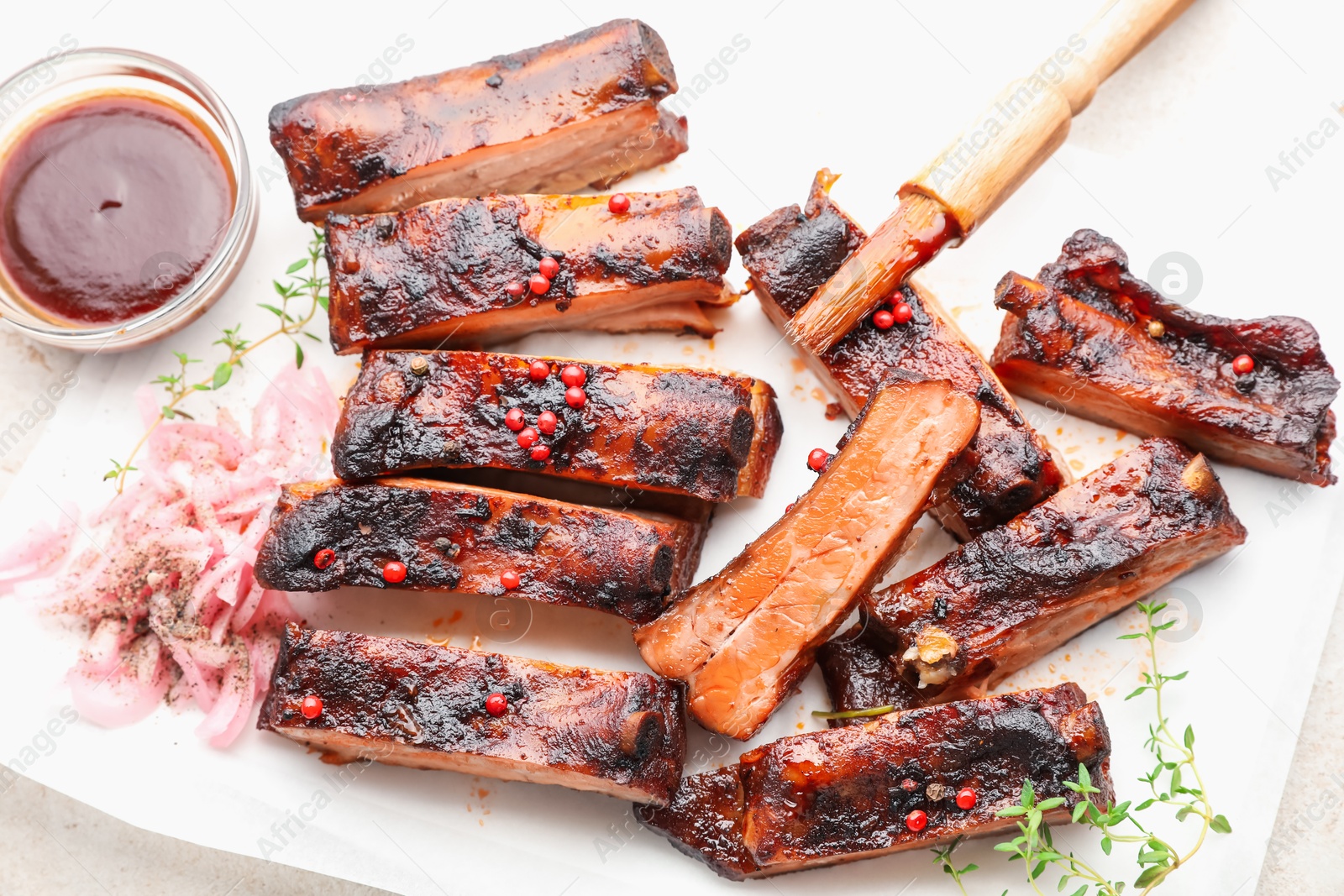 Photo of Delicious pork ribs, thyme, onion, sauce and brush on light table, flat lay