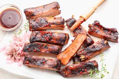 Photo of Delicious pork ribs, thyme, onion, sauce and brush on light table, flat lay