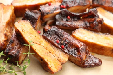 Photo of Delicious pork ribs and thyme on parchment paper, closeup