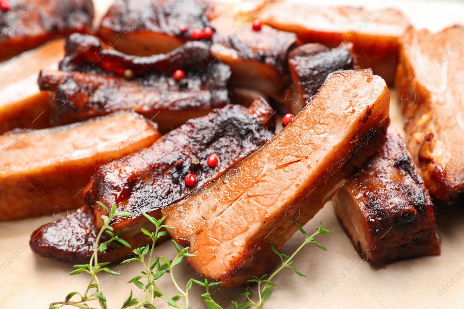 Photo of Delicious pork ribs and thyme on parchment paper, closeup