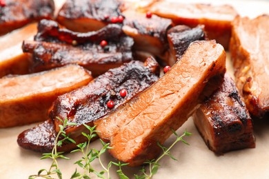 Photo of Delicious pork ribs and thyme on parchment paper, closeup