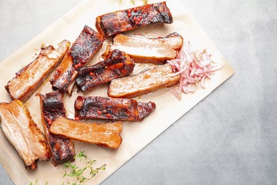 Photo of Delicious pork ribs, thyme and onion on grey textured table, top view. Space for text