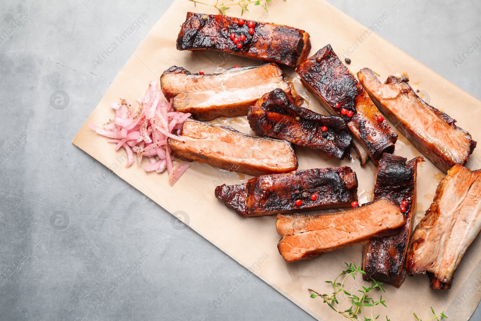 Delicious pork ribs, thyme and onion on grey textured table, top view. Space for text Photo of Delicious pork ribs, thyme and onion on grey textured table, top view. Space for text