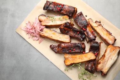 Photo of Delicious pork ribs, thyme and onion on grey textured table, top view. Space for text
