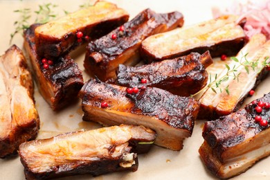 Photo of Delicious pork ribs and thyme on parchment paper, closeup