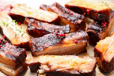 Photo of Delicious pork ribs and thyme on parchment paper, closeup
