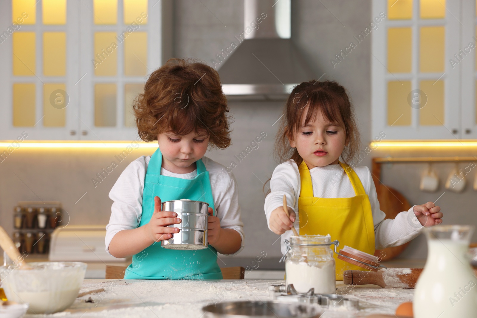 Cooking recipe. Cute children sieving flour at table in kitchen Photo of Cooking recipe. Cute children sieving flour at table in kitchen