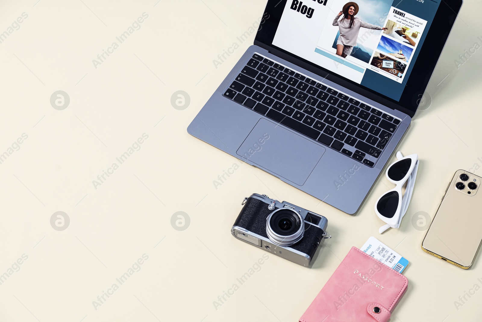 Laptop with travel blog web site, passport, flight ticket, vintage camera, smartphone and sunglasses on beige background, above view. Space for text Photo of Laptop with travel blog web site, passport, flight ticket, vintage camera, smartphone and sunglasses on beige background, above view. Space for text