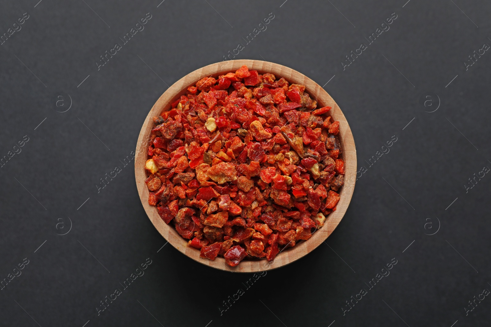 Red chili pepper flakes in bowl on dark table, top view Photo of Red chili pepper flakes in bowl on dark table, top view