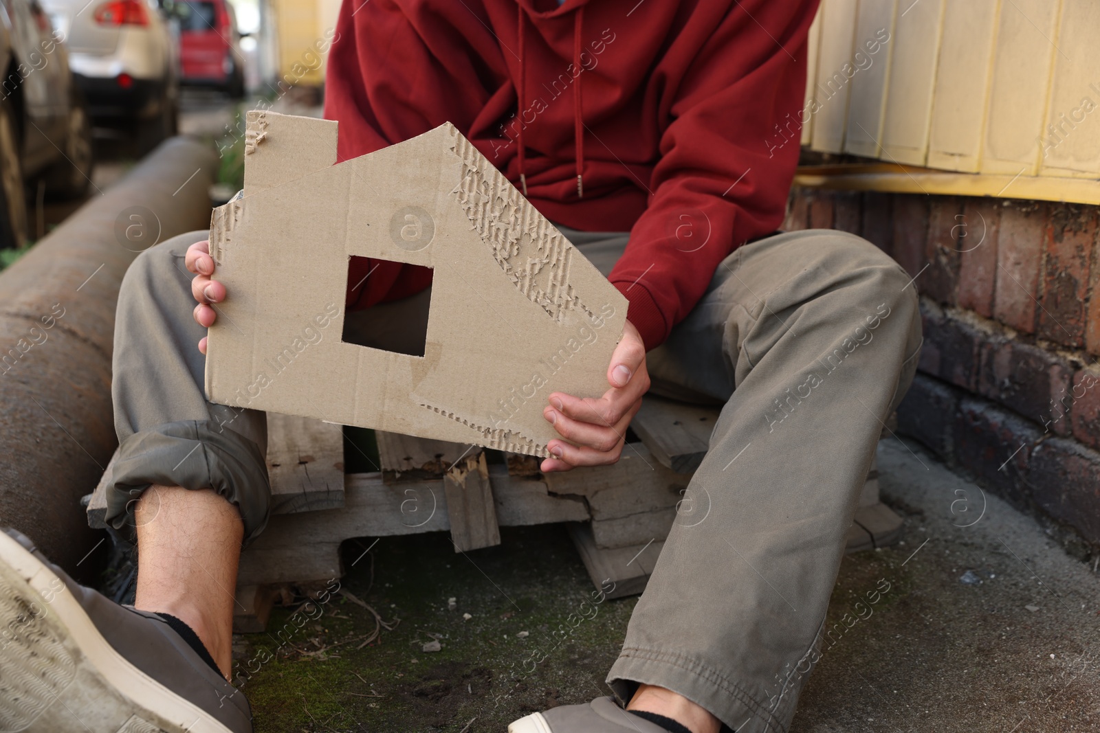 Homeless man with carton house figure outdoors, closeup Photo of Homeless man with carton house figure outdoors, closeup