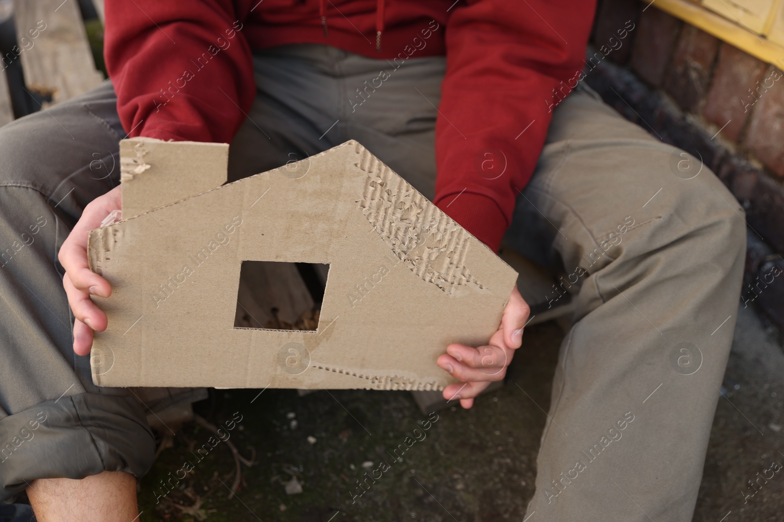 Homeless man with carton house figure outdoors, closeup Photo of Homeless man with carton house figure outdoors, closeup