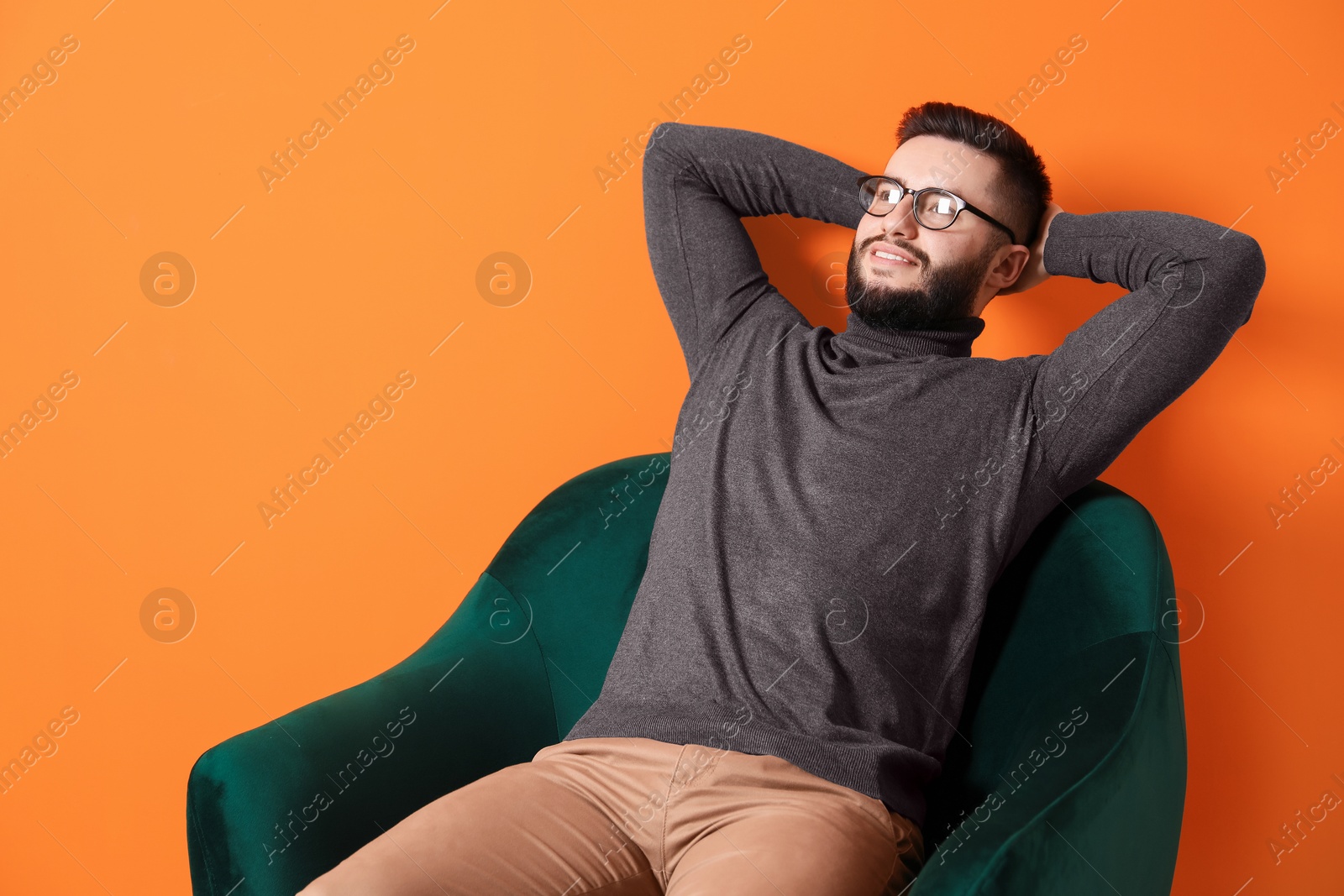 Smiling man relaxing on armchair against orange background Photo of Smiling man relaxing on armchair against orange background