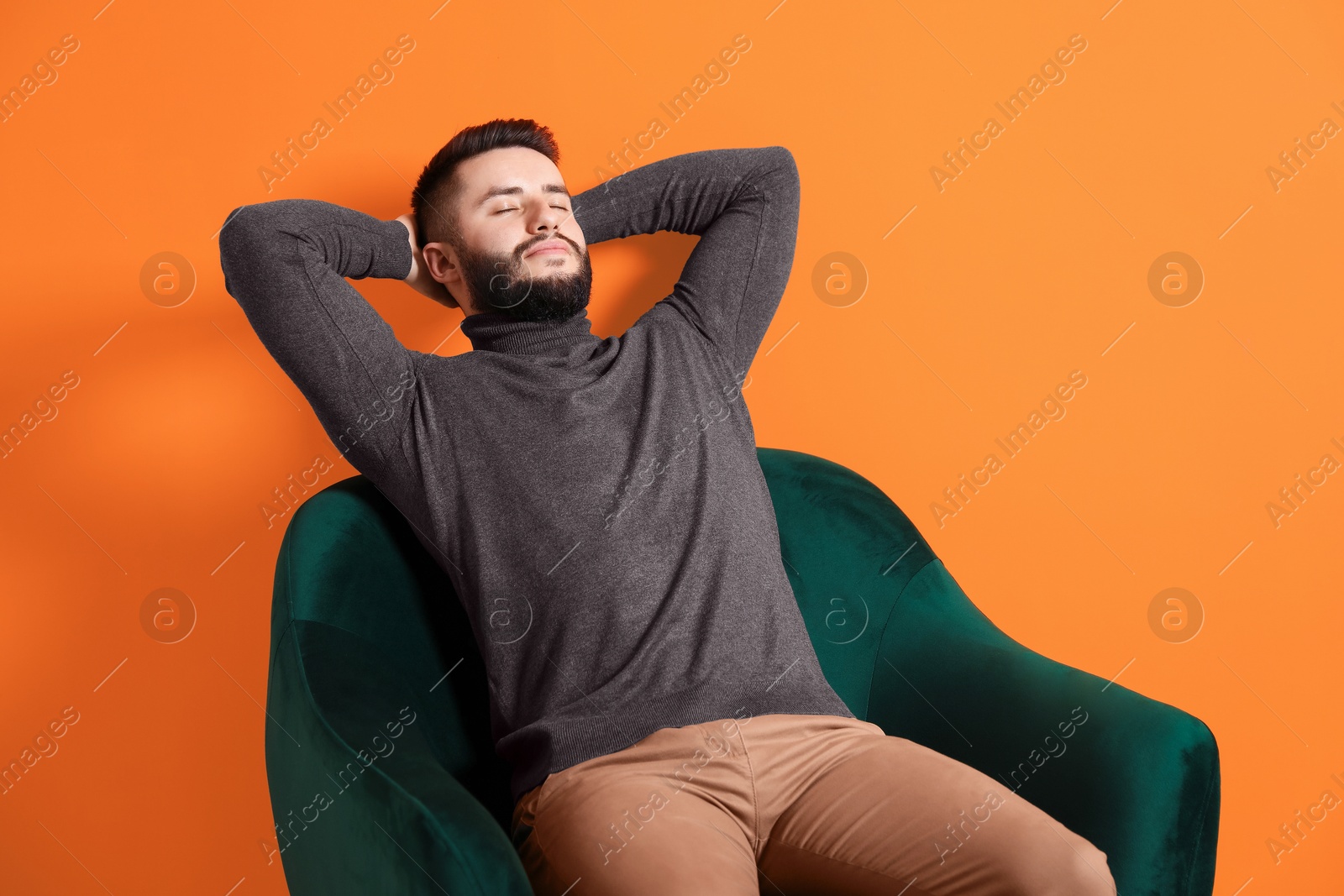 Photo of Handsome man relaxing on armchair against orange background