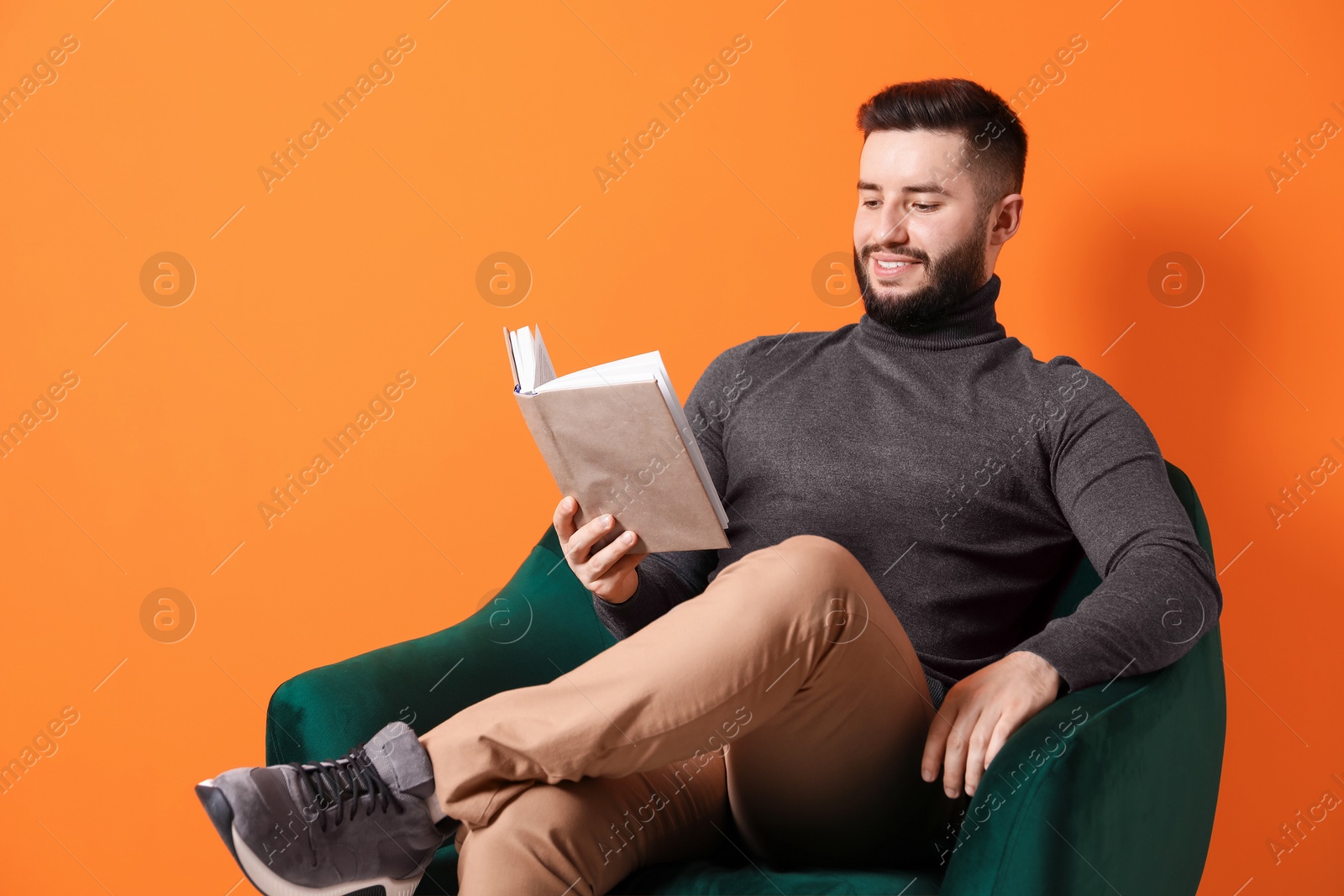 Smiling man with book relaxing on armchair against orange background Photo of Smiling man with book relaxing on armchair against orange background