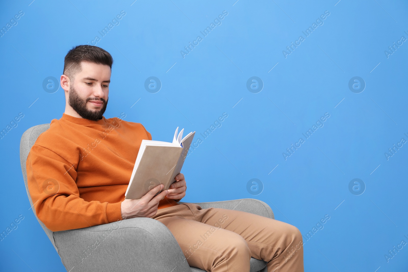 Photo of Handsome man with book relaxing on armchair against blue background. Space for text