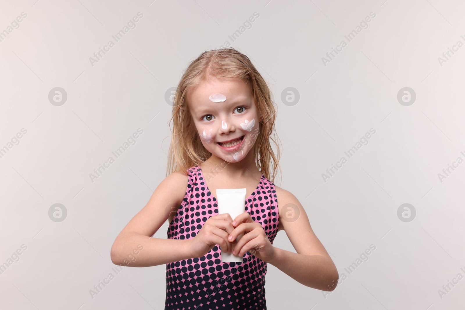 Smiling little girl with tube of sun protection product on grey background Photo of Smiling little girl with tube of sun protection product on grey background