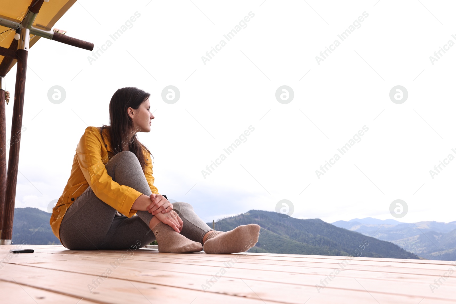 Young woman sitting on porch in mountains, space for text. Active tourism Photo of Young woman sitting on porch in mountains, space for text. Active tourism