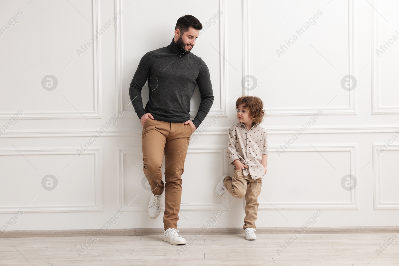 Happy father and his son near white wall indoors Photo of Happy father and his son near white wall indoors