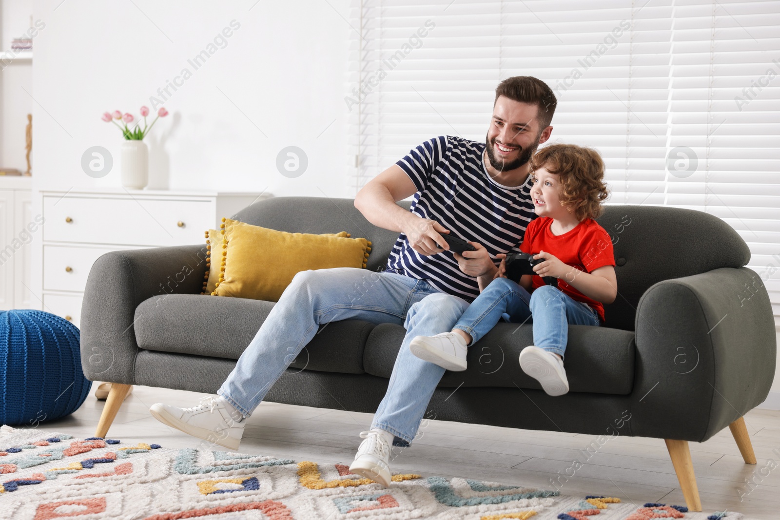 Happy father and his son playing with game controllers together on sofa at home Photo of Happy father and his son playing with game controllers together on sofa at home