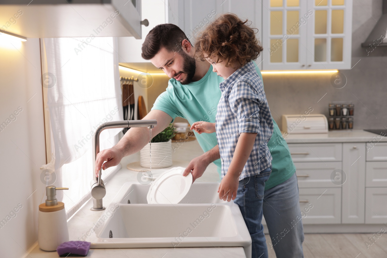 Father and his son washing dishes together in kitchen at home Photo of Father and his son washing dishes together in kitchen at home