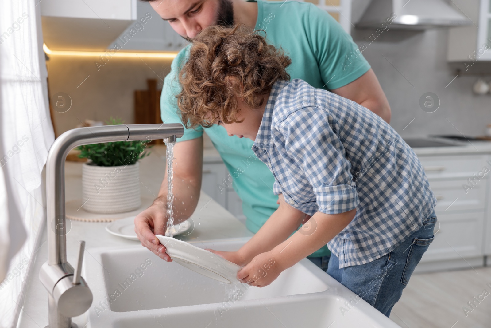 Father and his son washing dishes together in kitchen at home Photo of Father and his son washing dishes together in kitchen at home