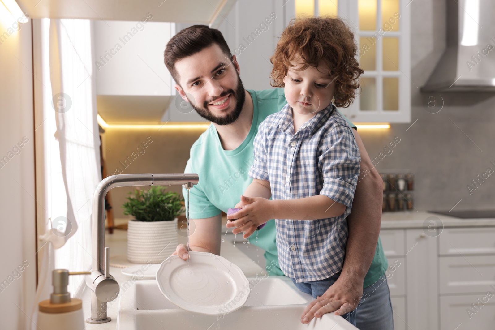 Father and his son washing dishes together in kitchen at home Photo of Father and his son washing dishes together in kitchen at home