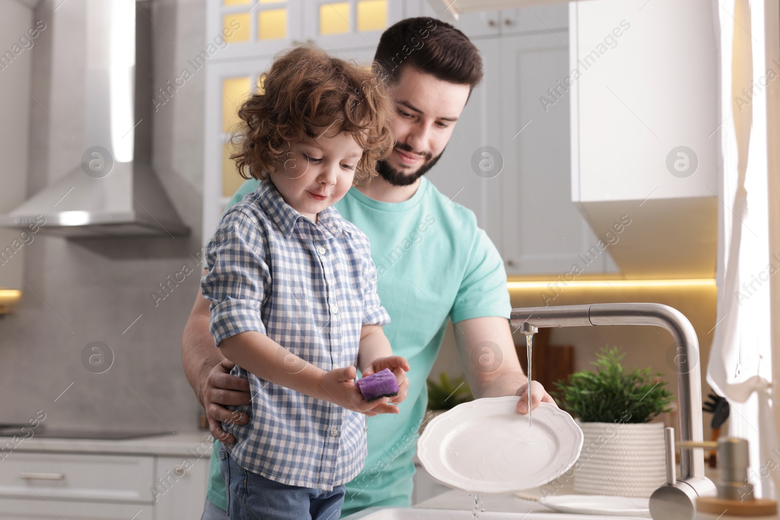 Father and his son washing dishes together in kitchen at home Photo of Father and his son washing dishes together in kitchen at home