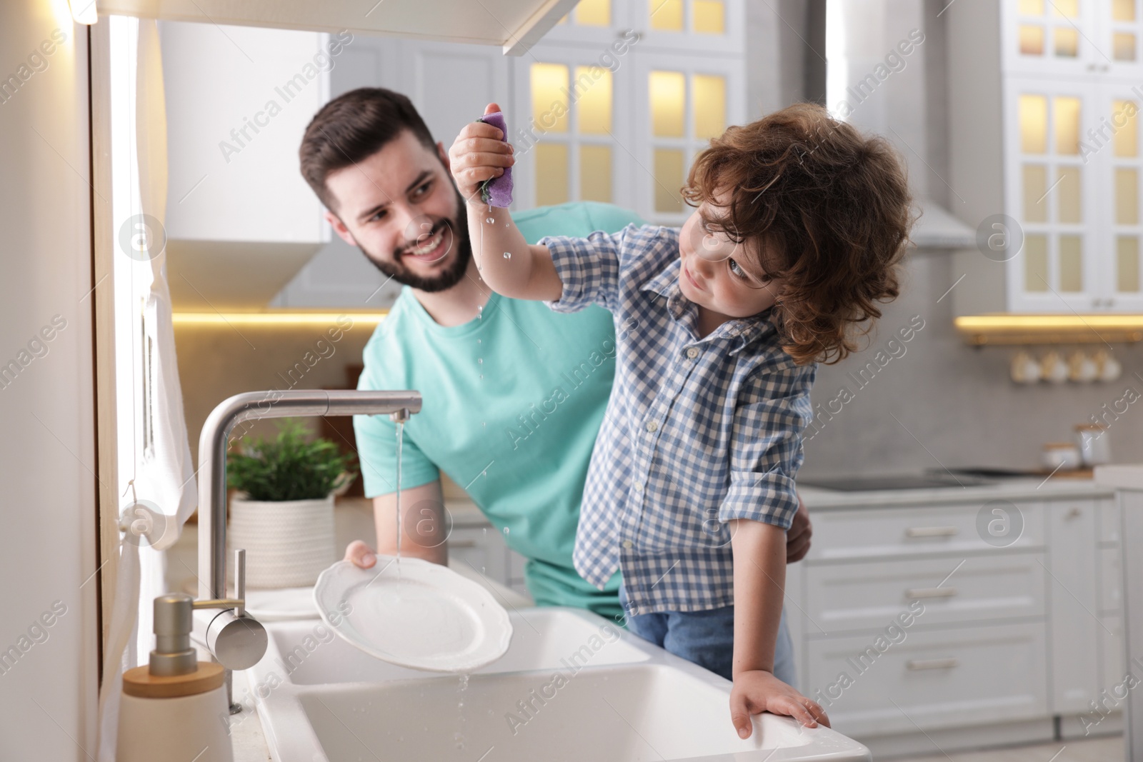 Father and his son washing dishes together in kitchen at home Photo of Father and his son washing dishes together in kitchen at home