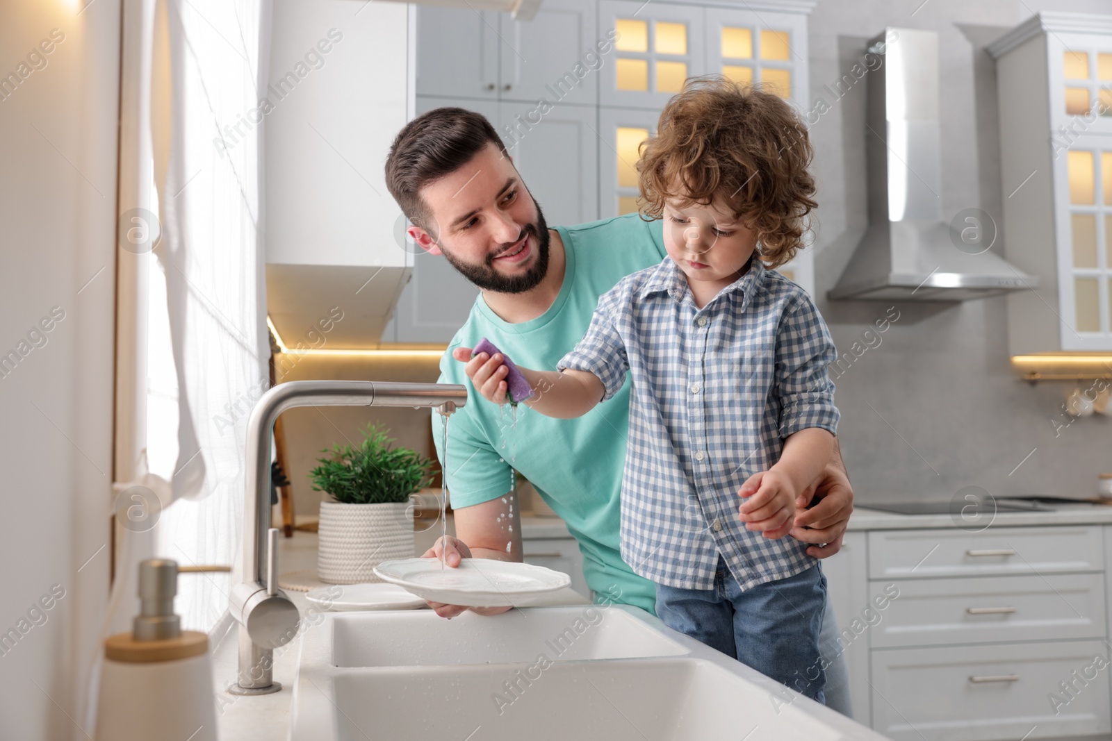 Father and his son washing dishes together in kitchen at home Photo of Father and his son washing dishes together in kitchen at home