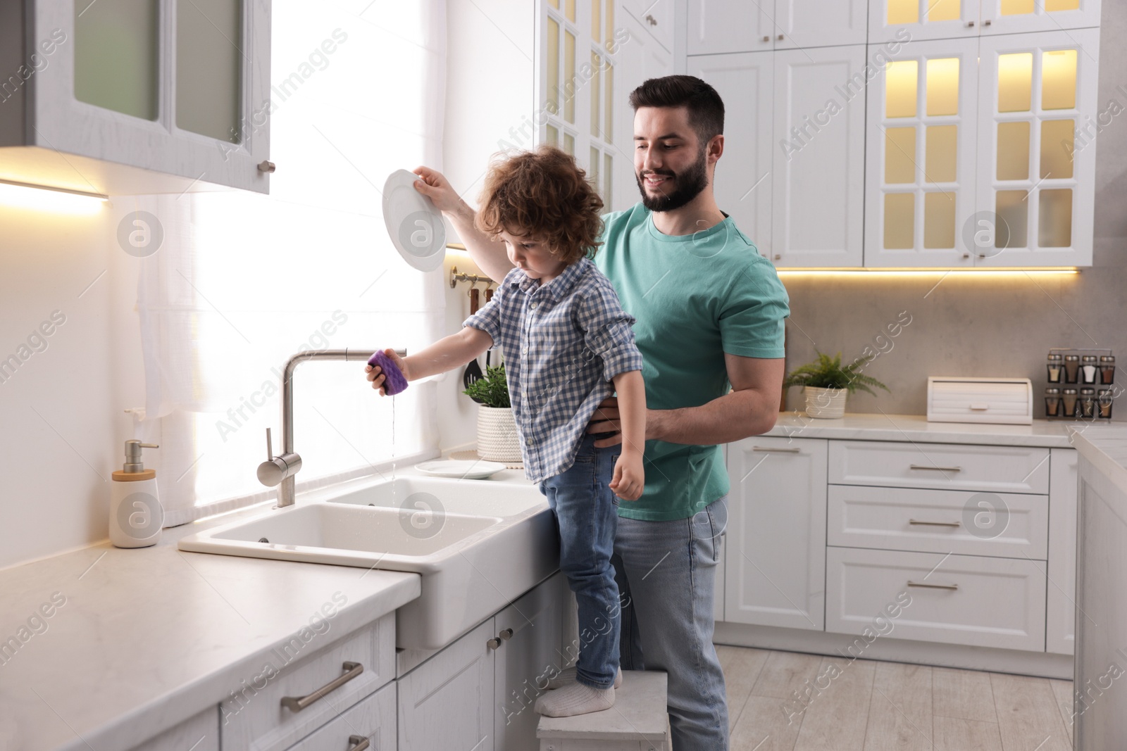Father and his son washing dishes together in kitchen at home Photo of Father and his son washing dishes together in kitchen at home