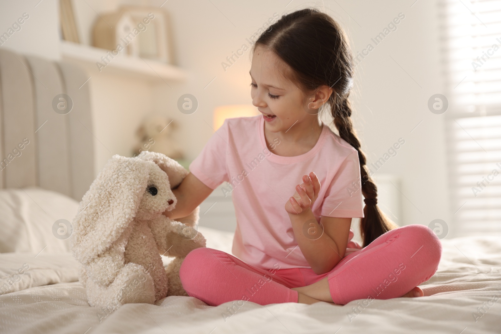 Cute girl with toy bunny on bed at home Photo of Cute girl with toy bunny on bed at home
