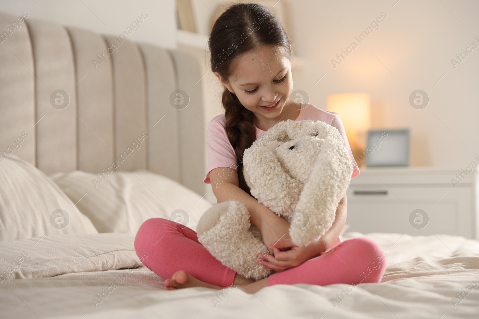 Cute girl with toy bunny on bed at home Photo of Cute girl with toy bunny on bed at home