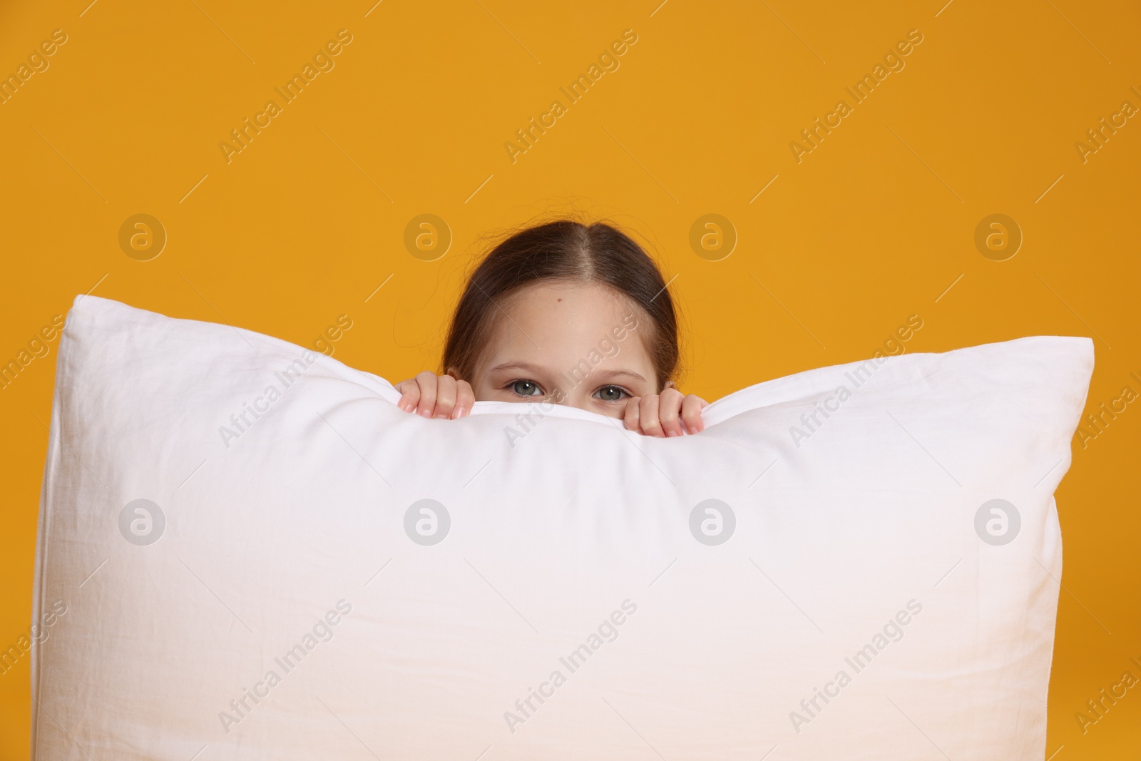 Cute girl with pillow on orange background Photo of Cute girl with pillow on orange background
