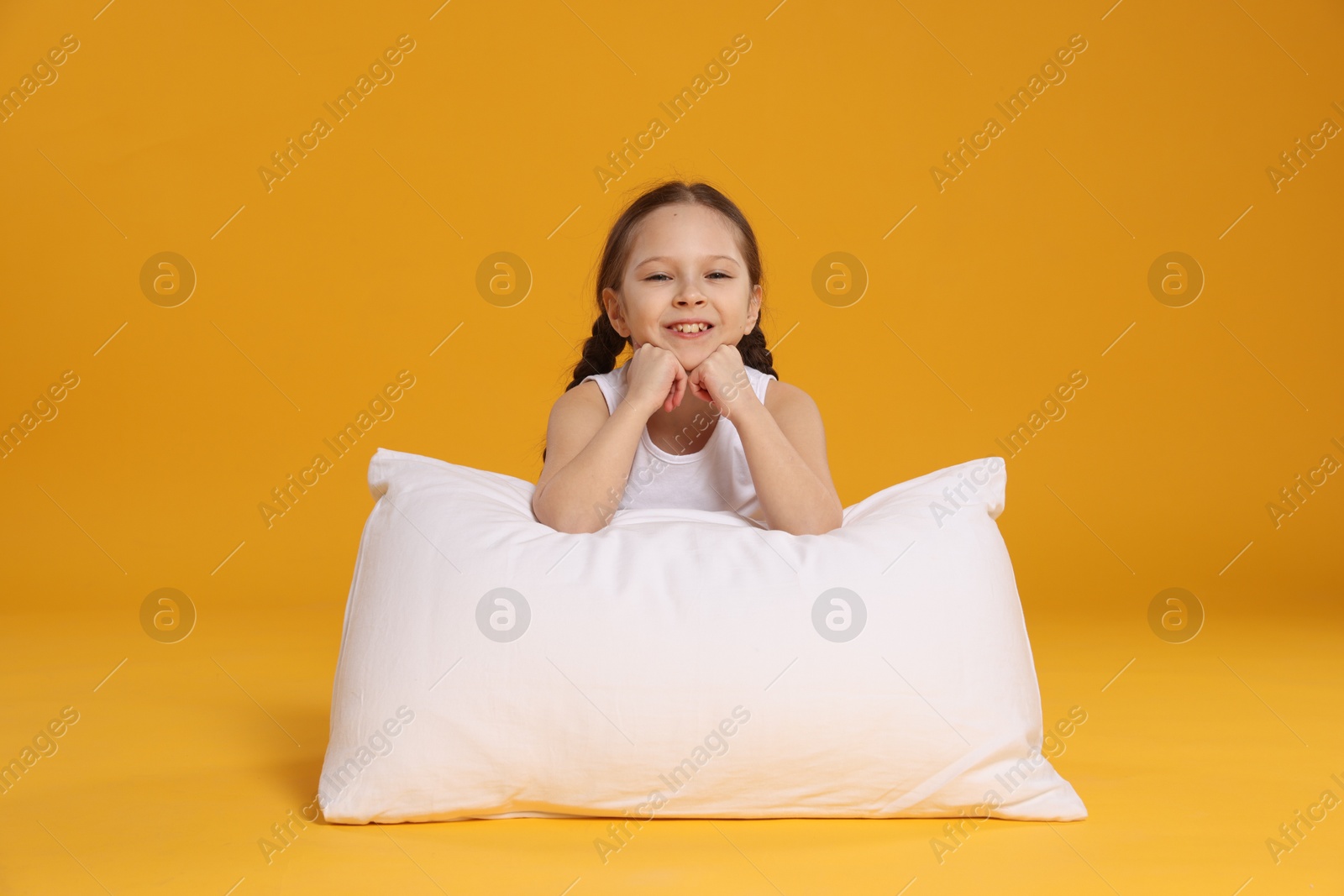 Cute girl with pillow on orange background Photo of Cute girl with pillow on orange background