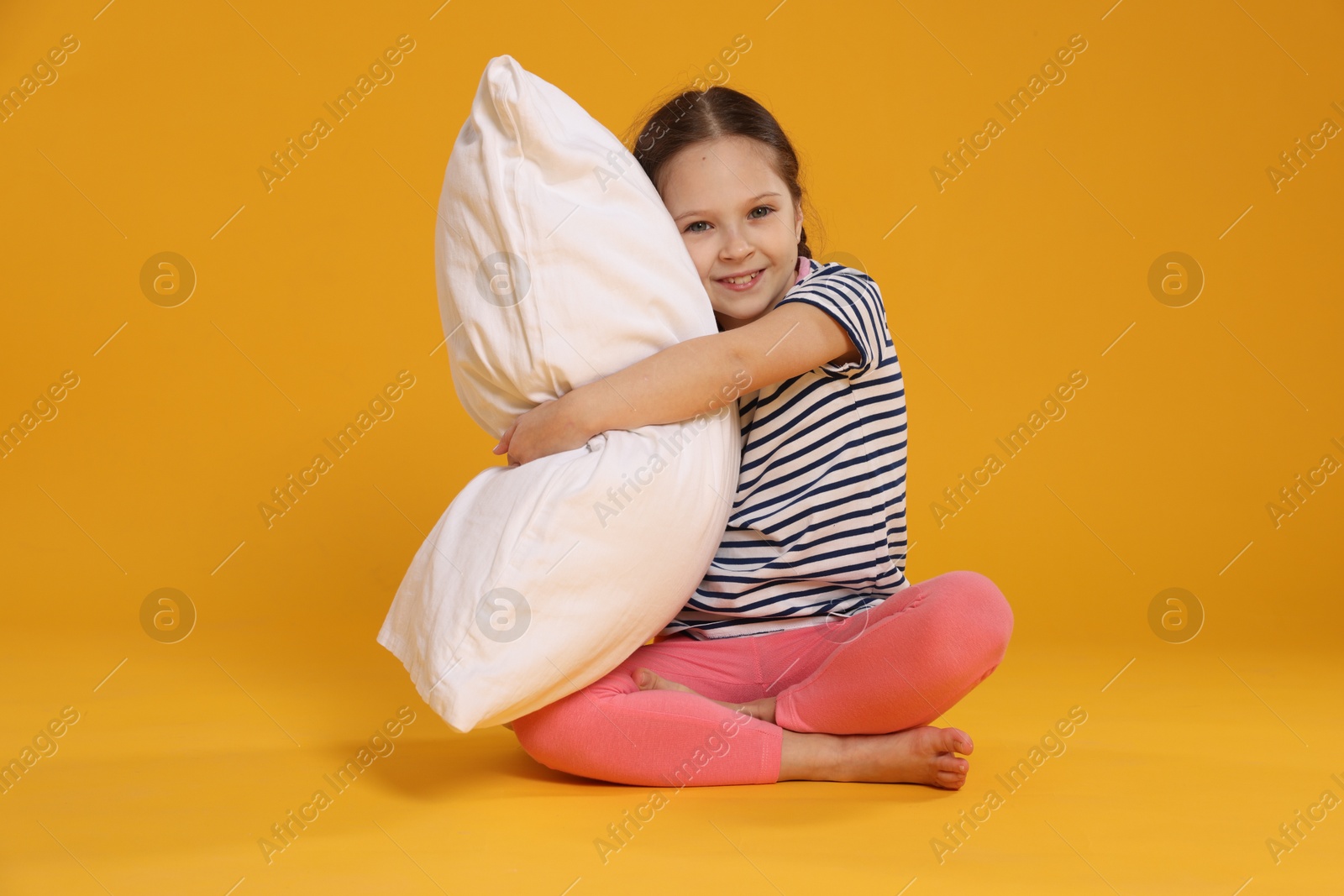 Cute girl with pillow on orange background Photo of Cute girl with pillow on orange background