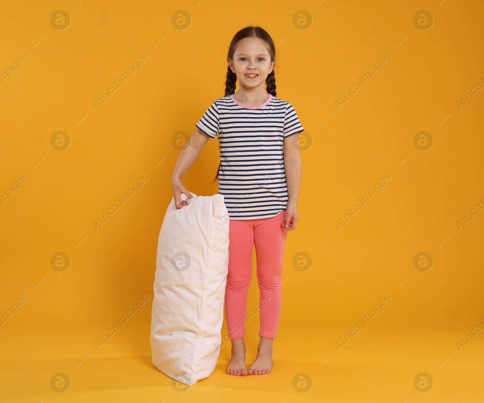 Cute girl with pillow on orange background Photo of Cute girl with pillow on orange background