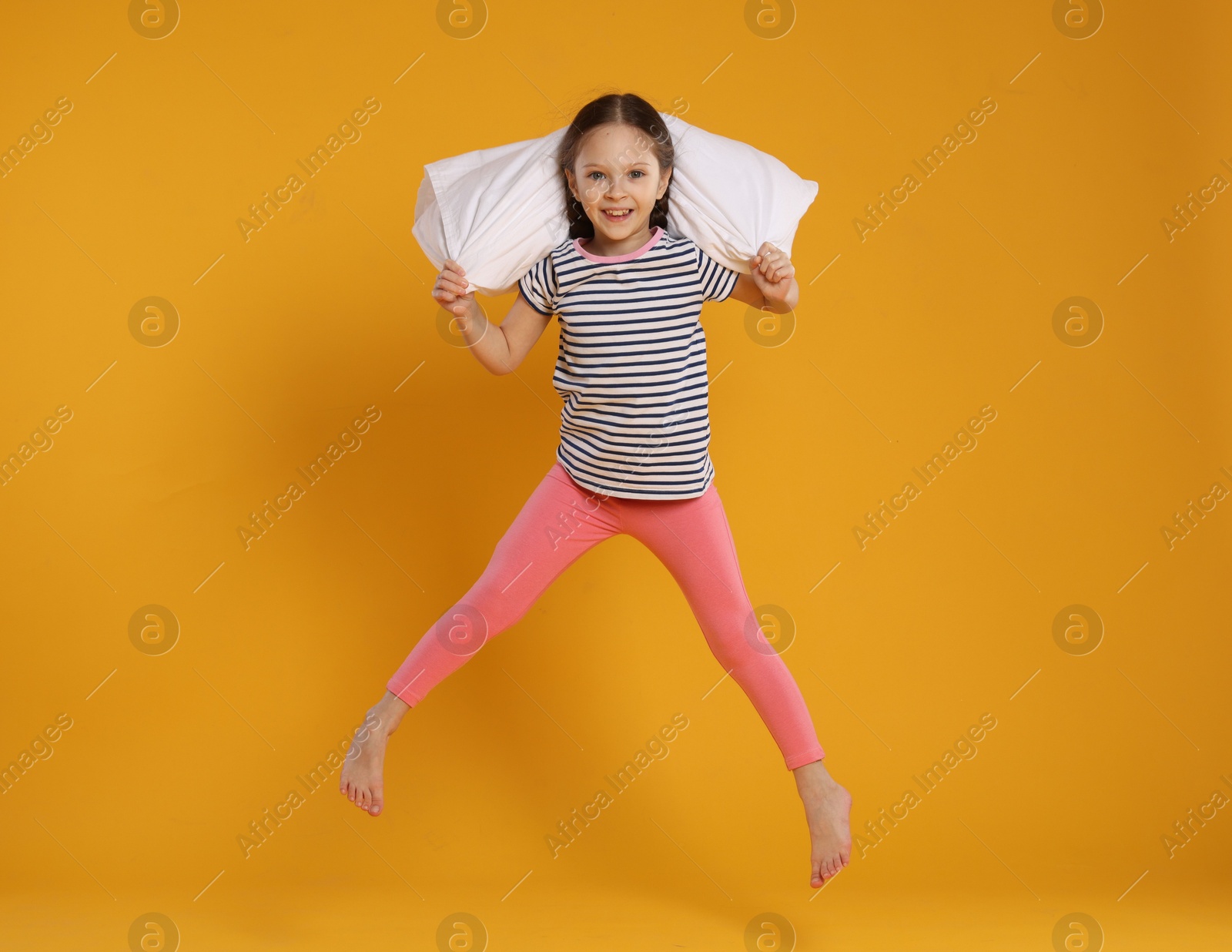 Cute girl with pillow jumping on orange background Photo of Cute girl with pillow jumping on orange background
