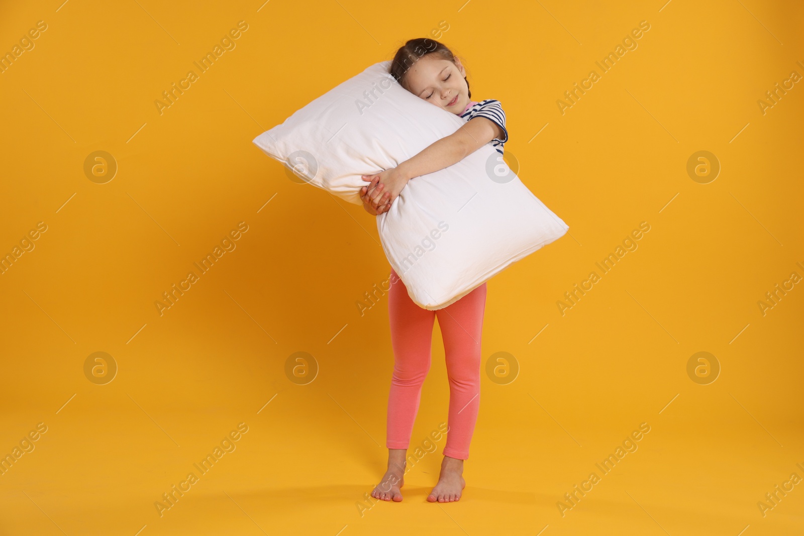 Cute girl with pillow on orange background Photo of Cute girl with pillow on orange background