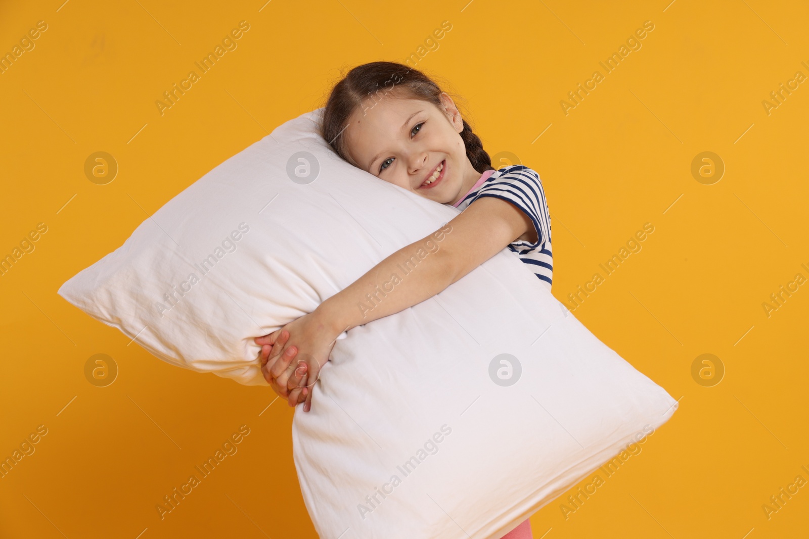 Cute girl with pillow on orange background Photo of Cute girl with pillow on orange background