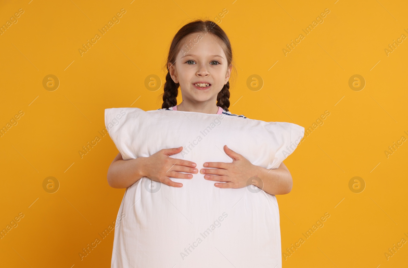 Cute girl with pillow on orange background Photo of Cute girl with pillow on orange background
