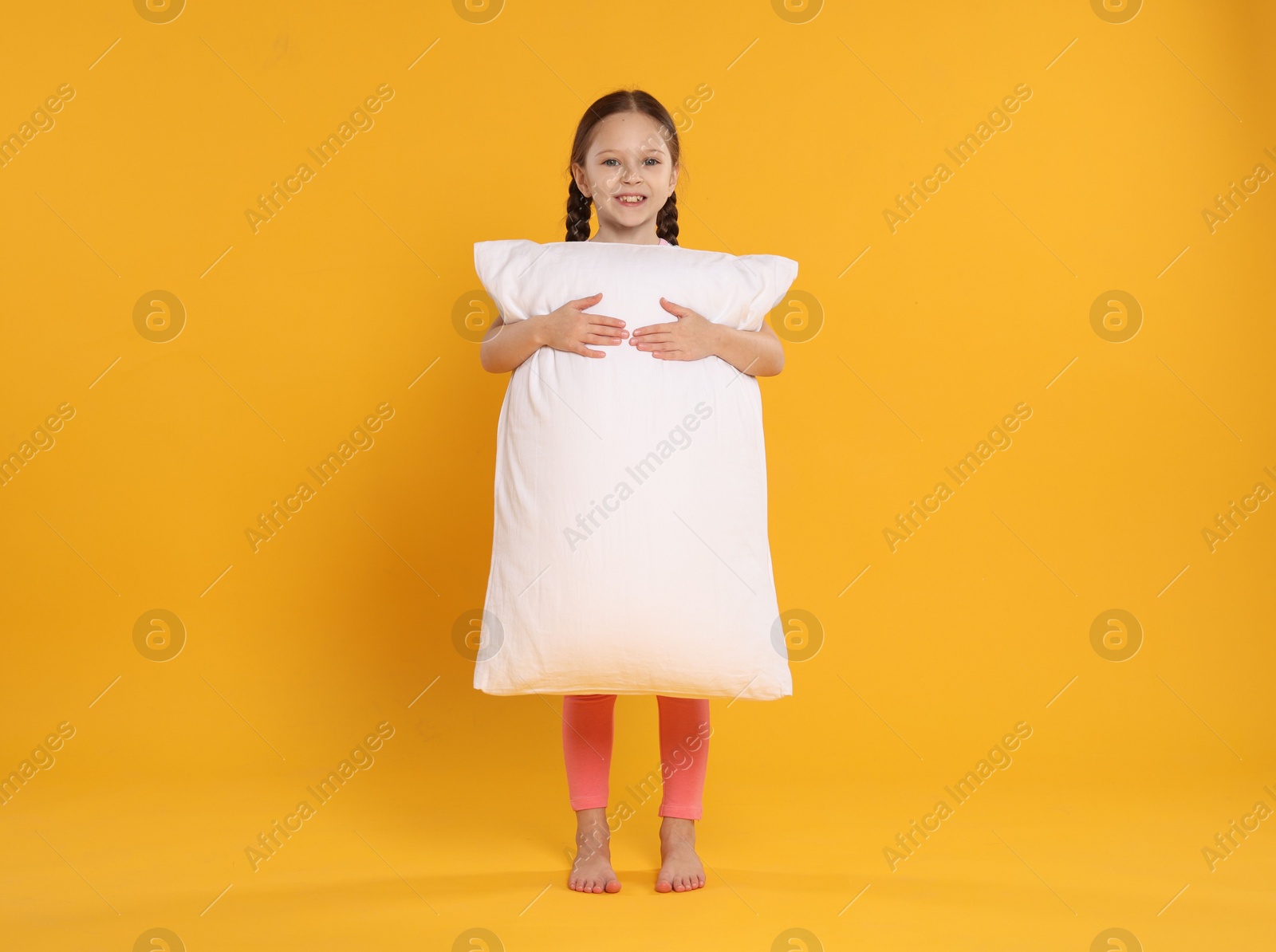 Cute girl with pillow on orange background Photo of Cute girl with pillow on orange background