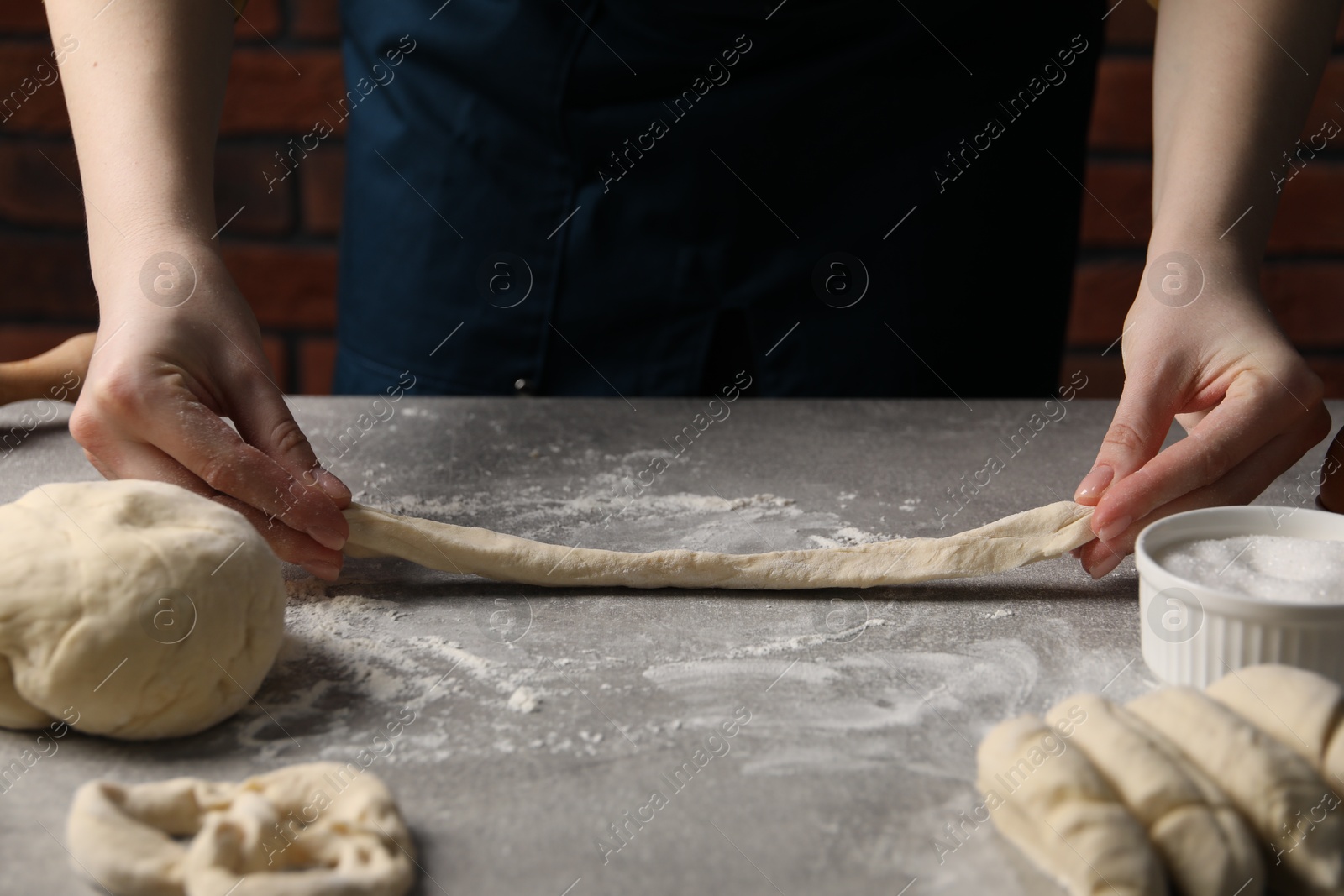 Woman making pretzel at light grey table, closeup Photo of Woman making pretzel at light grey table, closeup